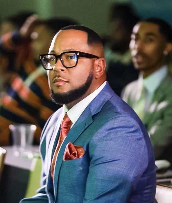 Richard Hall Jr. in a blue suit and glasses, seated at an event